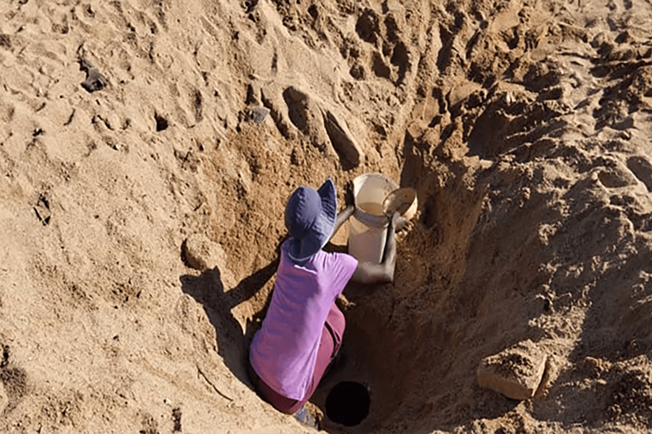 A woman crouching in a dirt pit in Zimbabwe.