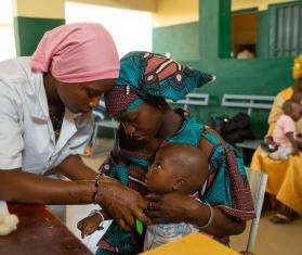 A mother holder her child while he is examined by a nurse in Niono, Mali 