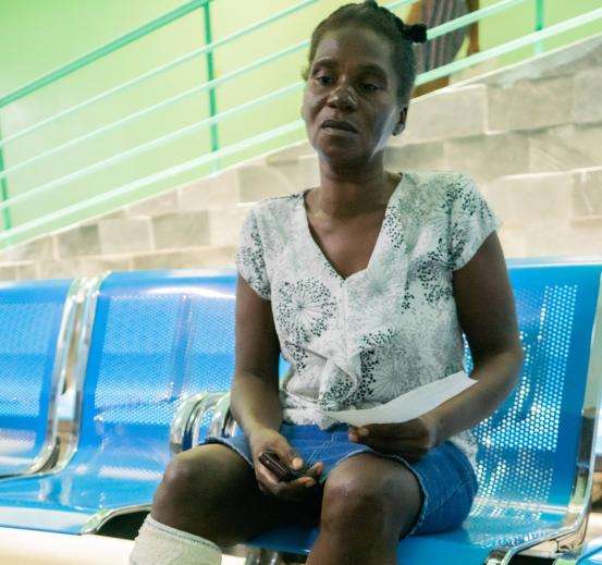 A woman with wound dressing on her leg sits in a hospital waiting room. 