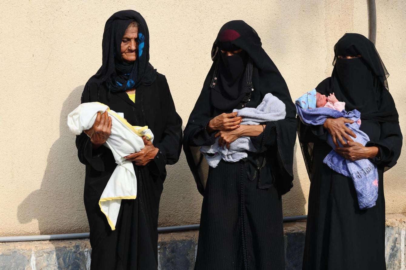 Three women carry babies outside Abs General Hospital in Yemen.