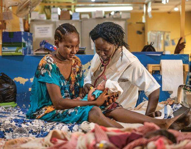 An MSF nurse and patient sit on a hospital bed with a newborn baby in Aweil, South Sudan.