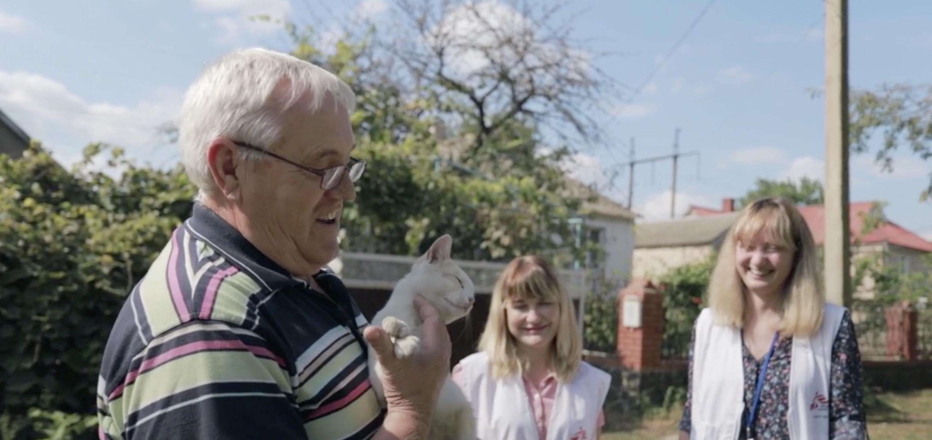 Older man holding a cat, smiling, surrounded by MSF staff