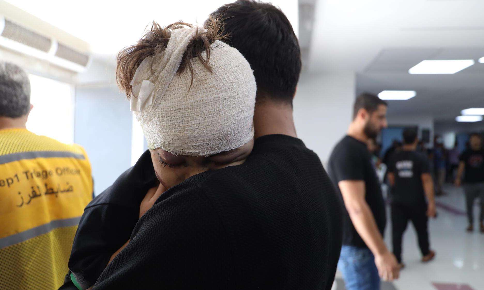 An injured boy rests his bandaged head on his father's shoulder at Al Shifa Hospital in Gaza