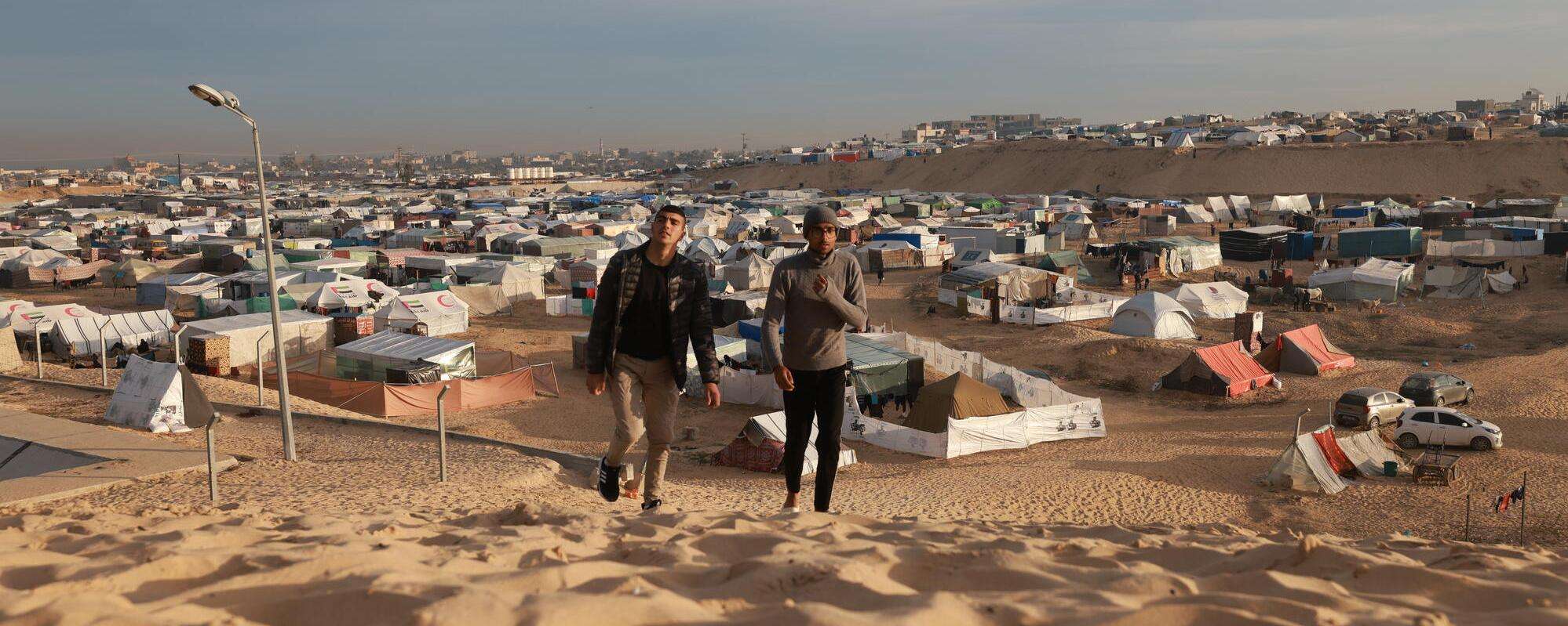 Palestinian men walk on a dune near an informal camp for displaced Palestinians in the coastal area of Mawasi Rafah, in the south of the Gaza Strip.