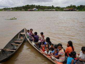 Indigenous people sit on a long canoe on a brown river in Venezuela under cloudy sky