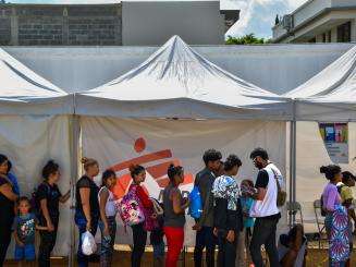 A group of migrants standing on a line under an MSF tent in Danlí, Honduras.