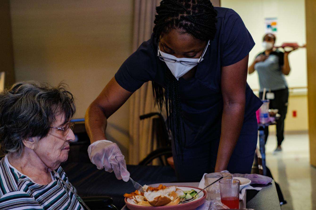 A facility staff member helps a resident eat lunch in her room at Focused Care at Beechnut, a long-term nursing care facility in Houston, Texas, that was affected by the global COVID-19 pandemic.