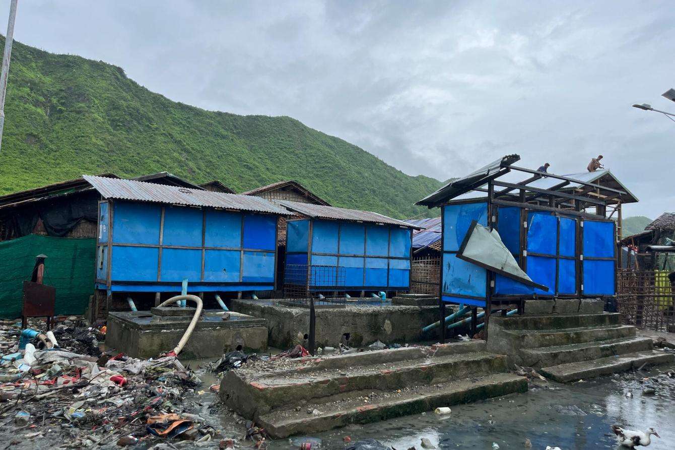 Blue buildings with tin roofs surrounded by flooding with a mountain in the background.
