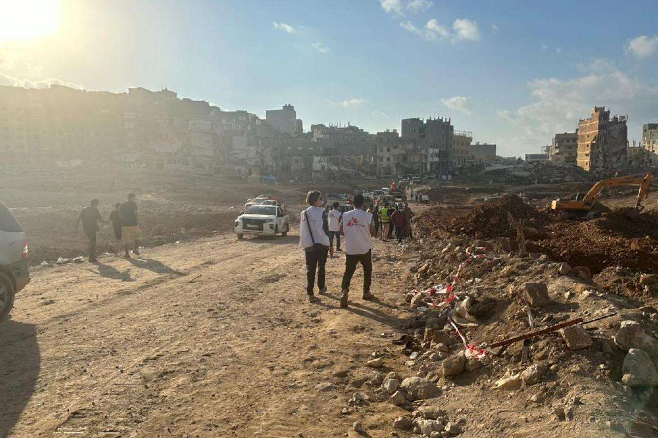 Several people in MSF shirts walking around a scene with destroyed buildings in Derna.