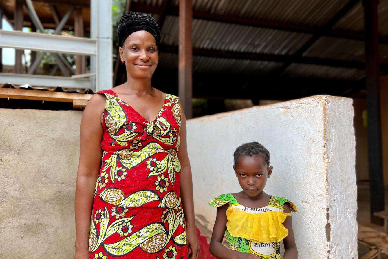 A mother in a red dress with her young daughter in a yellow dress, patients at the Kidjigra health center in Bambari, Central African Republic