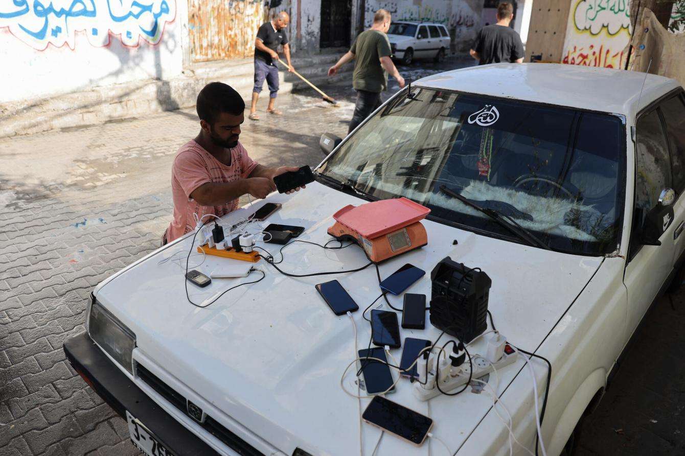 A Palestinian man charges his phone on the hood of a car in Gaza, where electricity has been cut off by Israel.