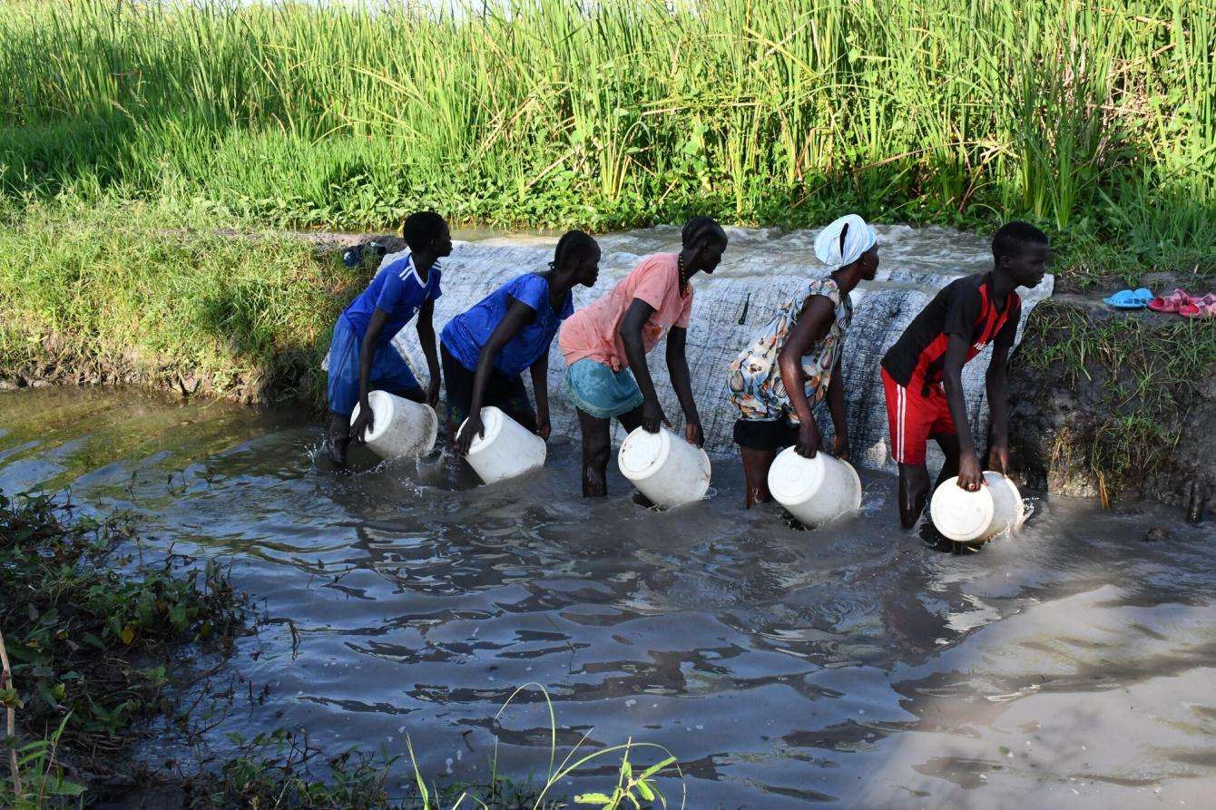 People fetch water from a flooded river with buckets in Old Fangak, South Sudan.