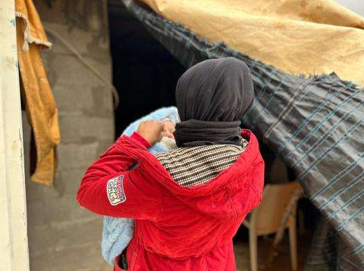 A Palestinian woman in a red jacket holds her child.