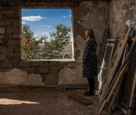 A Ukrainian woman looks out the window of a destroyed building.