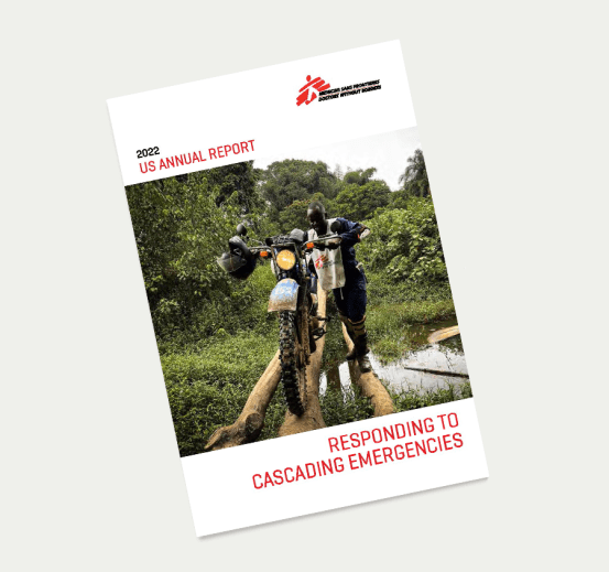 The cover of the 2022 annual report shows an MSF staff member carefully traversing a river, with his motorcycle rolling across narrow stilts laid over the water