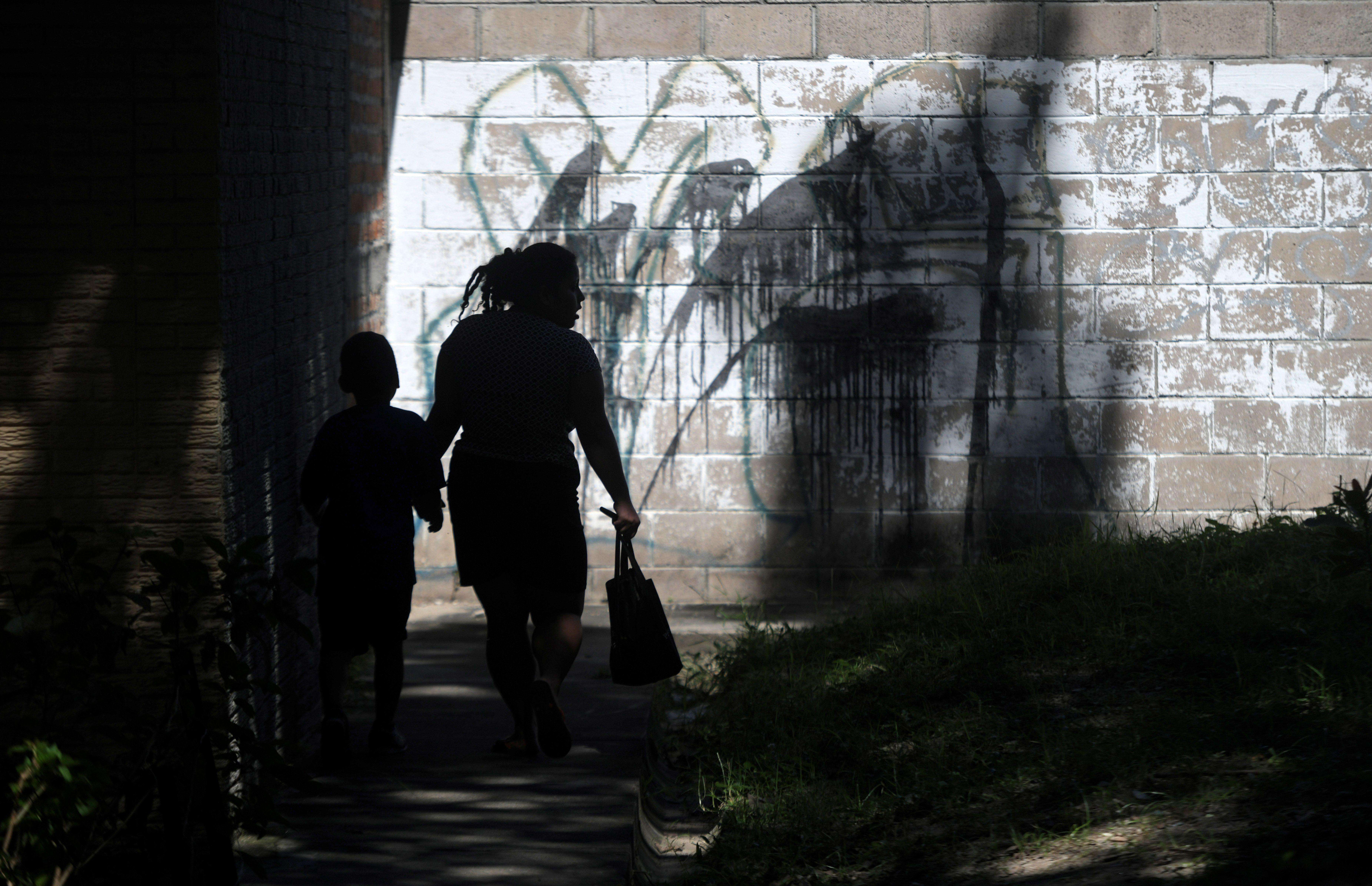 A woman and her son walk past graffiti referencing the M13 gang in Las Margaritas, Soyapango, El Salvador. 