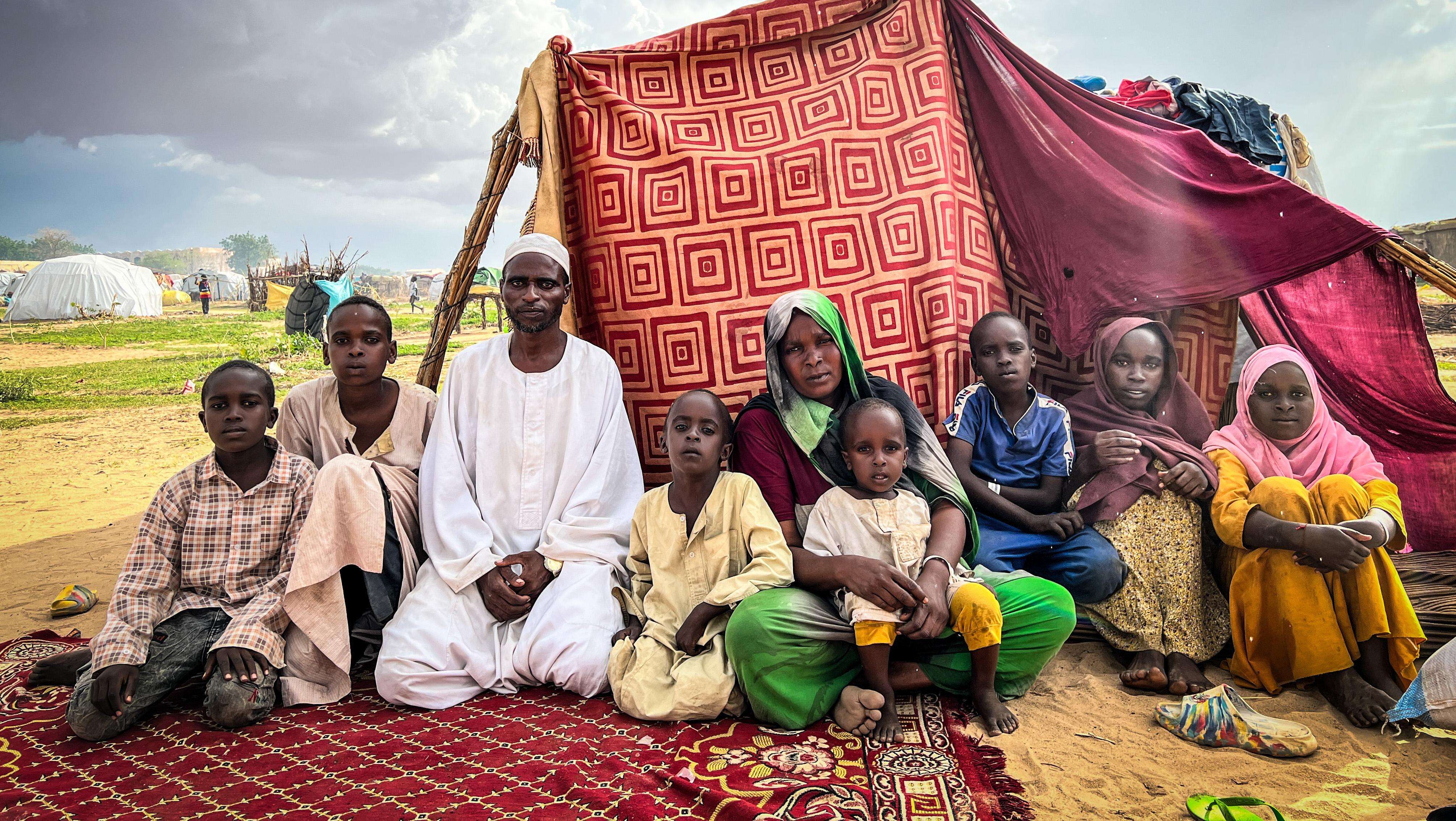 A family of Sudanese refugees sit in front of a makeshift tent in a refugee camp in Chad
