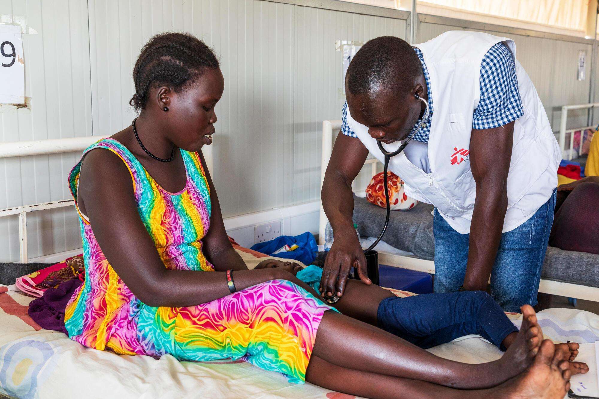 A woman on a bed is being examined by a doctor in the MSF hospital in Agok