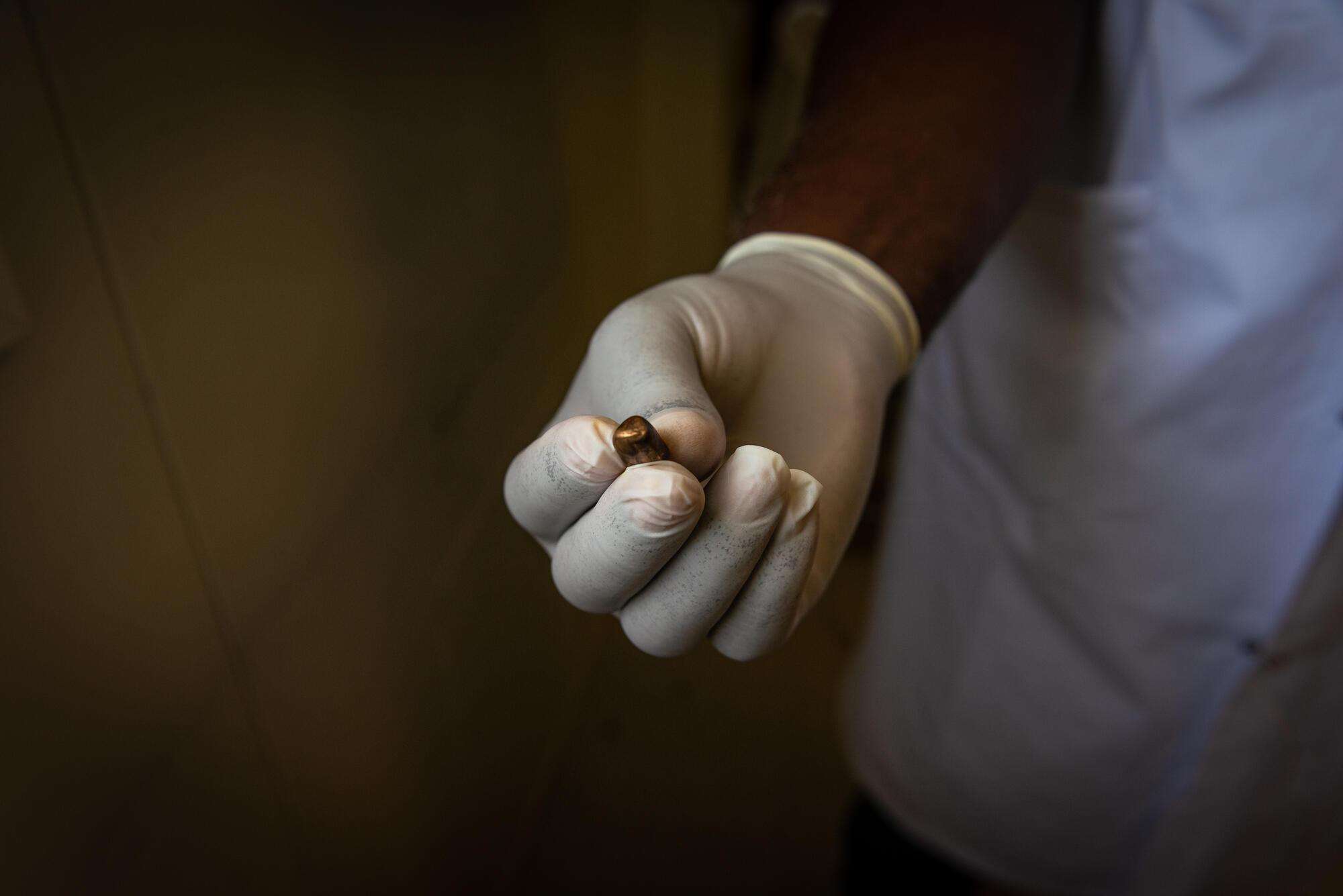 An MSF team member's hand in a surgical latex glove holding a bullet extracted from a patient in Haiti