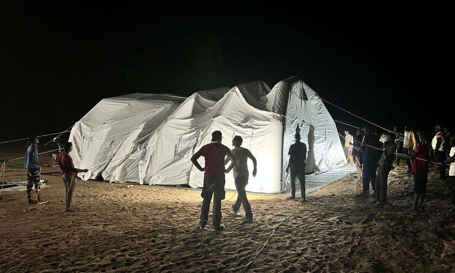 MSF aid workers with an inflatable tent hospital lit up in the night in Chad