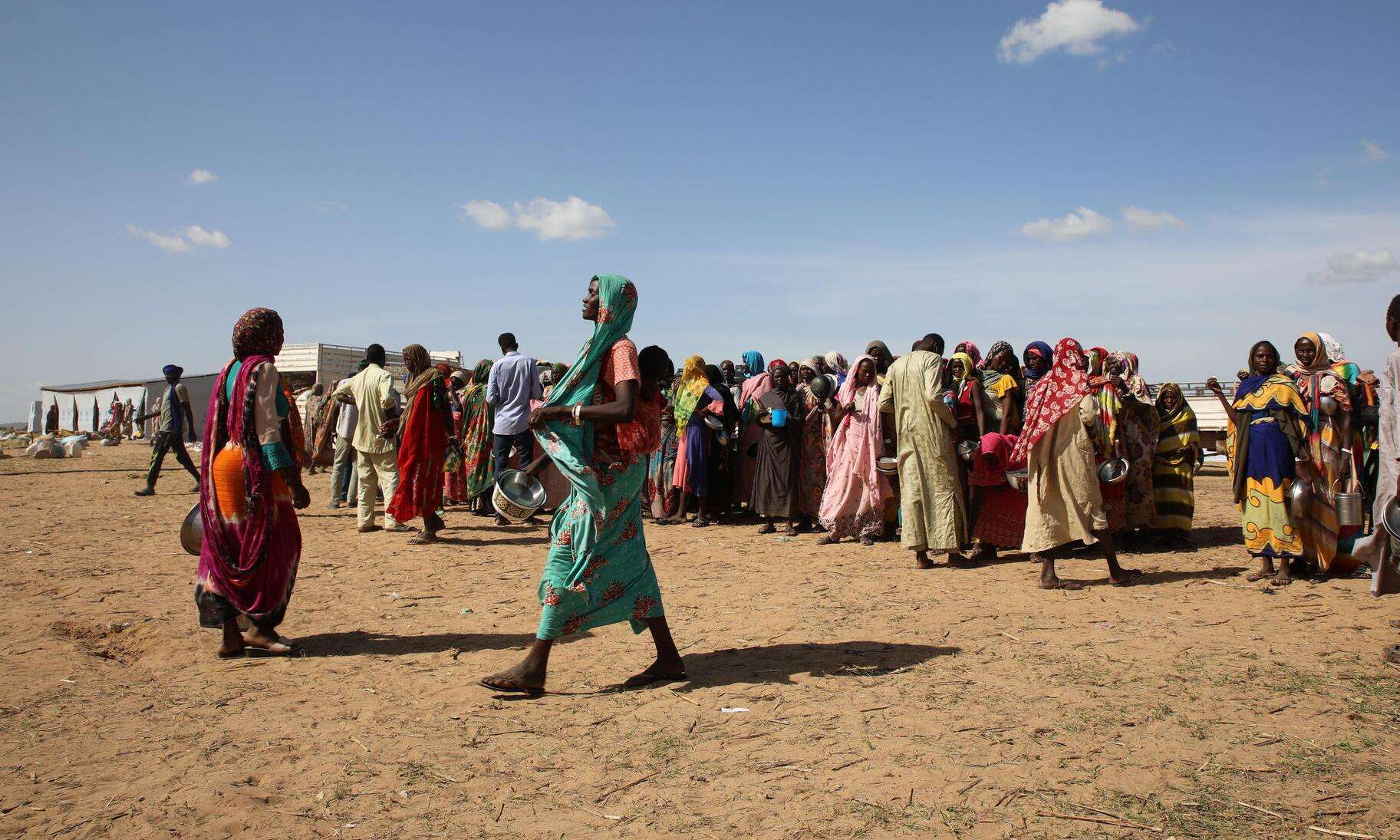 A woman in turquoise dress walks in front of crowd of people fleeing Sudan conflict to Chad 