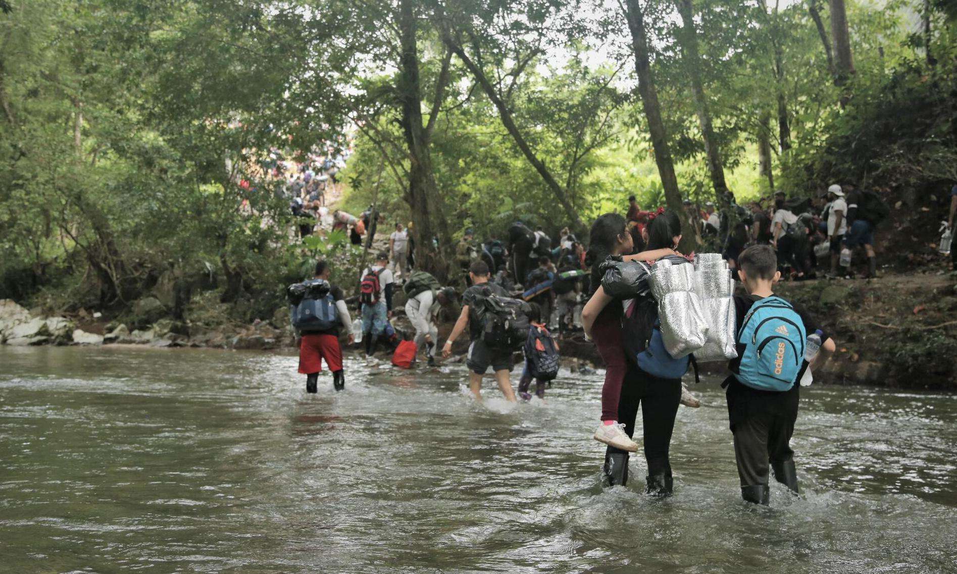 People migrating north walk across a river in the Darién Gap between Colombia and Panama.
