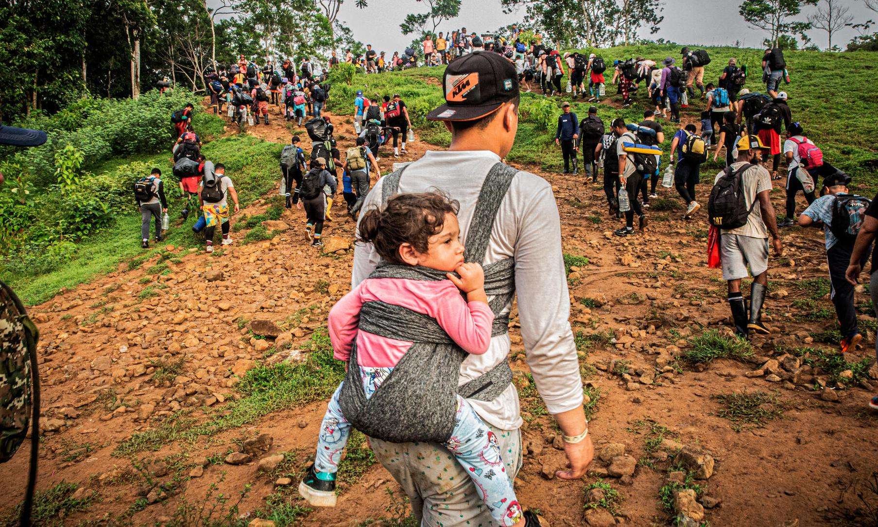 A migrant carries a child in a backpack as he crosses the Darién jungle between Colombia and Panama.