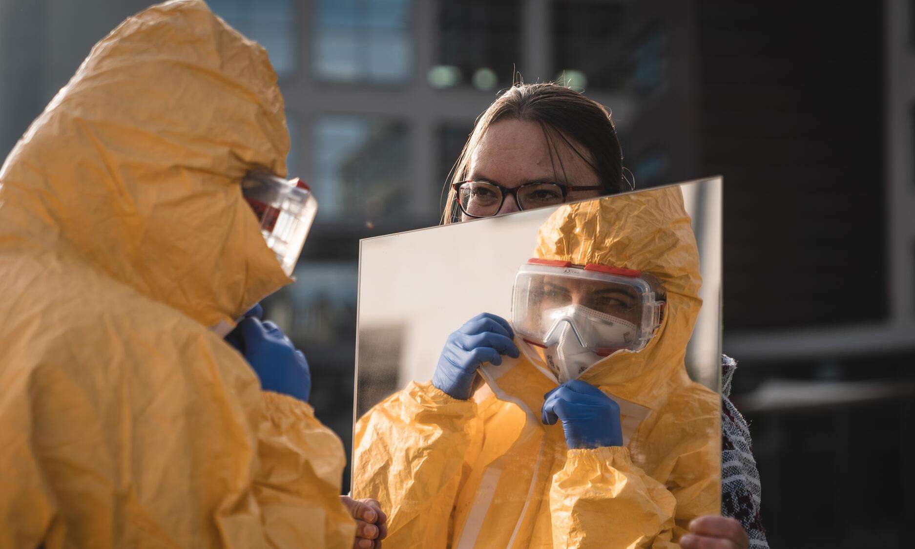 An MSF staff member holds a mirror in front of a person dressed in PPE in Belgium.