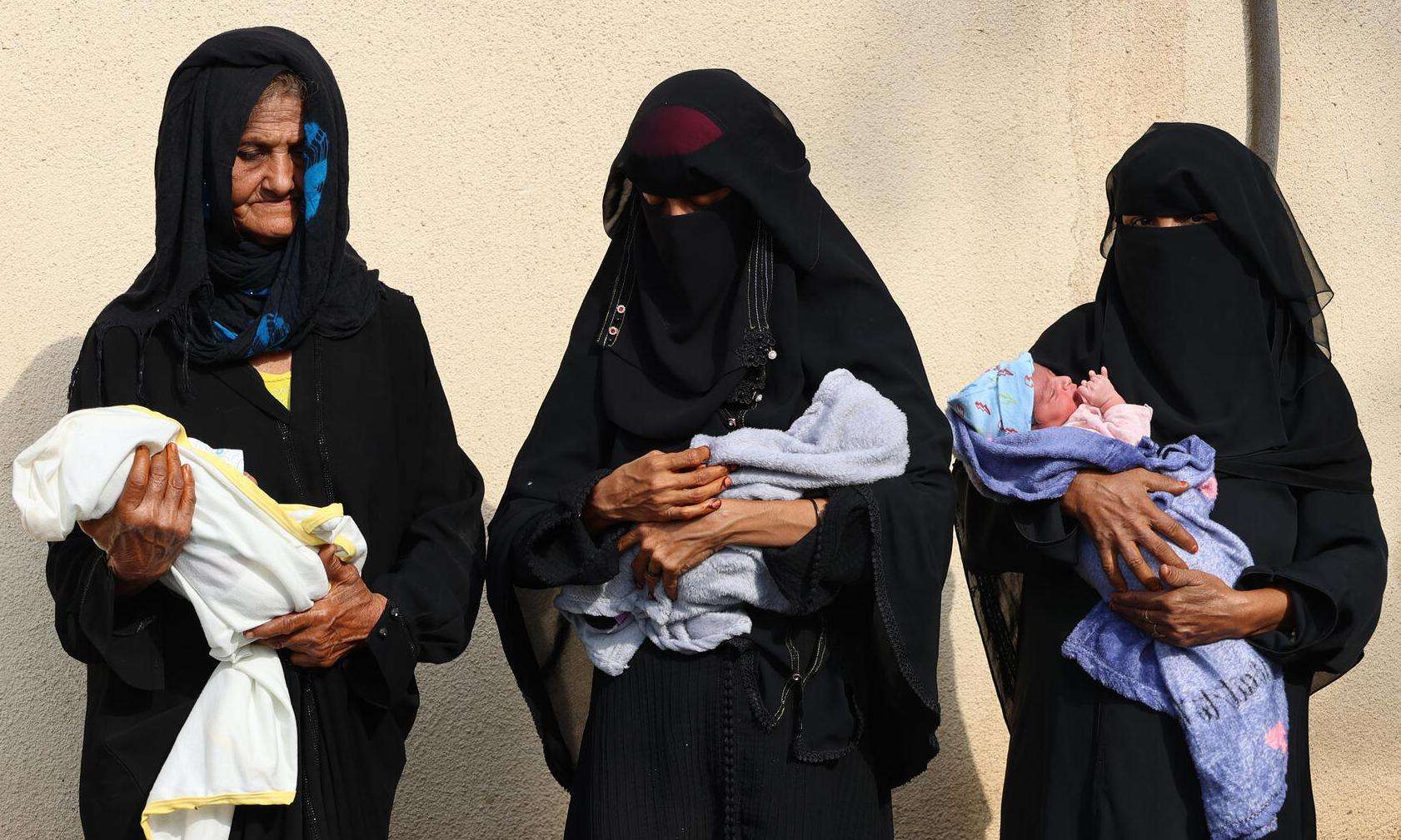 Three women carry babies outside Abs General Hospital in Yemen.