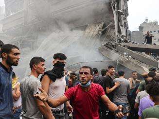 A group of Palestinians in front of smoke from a building destroyed by Israeli airstrikes in Gaza.