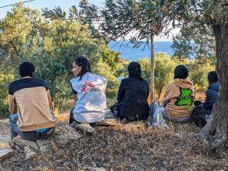 An MSF staff member sits with migrants on a hilltop in Lesvos, Greece.