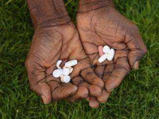Medication pills in the palms of a person's hand against grass.