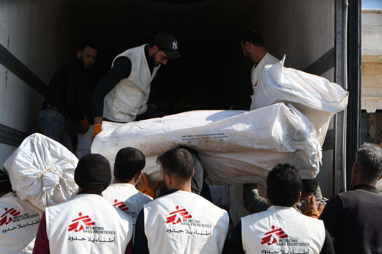 More than four men in MSF vests are helping to unload a truck full of tents and winter kits. We only see their backs as they work to pull the equipment off the truck.
