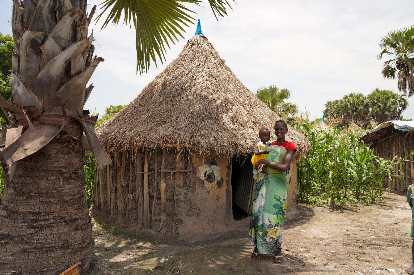 A mother holds her child, an MSF patient, in front of a straw hut in Jonglei state, South Sudan.