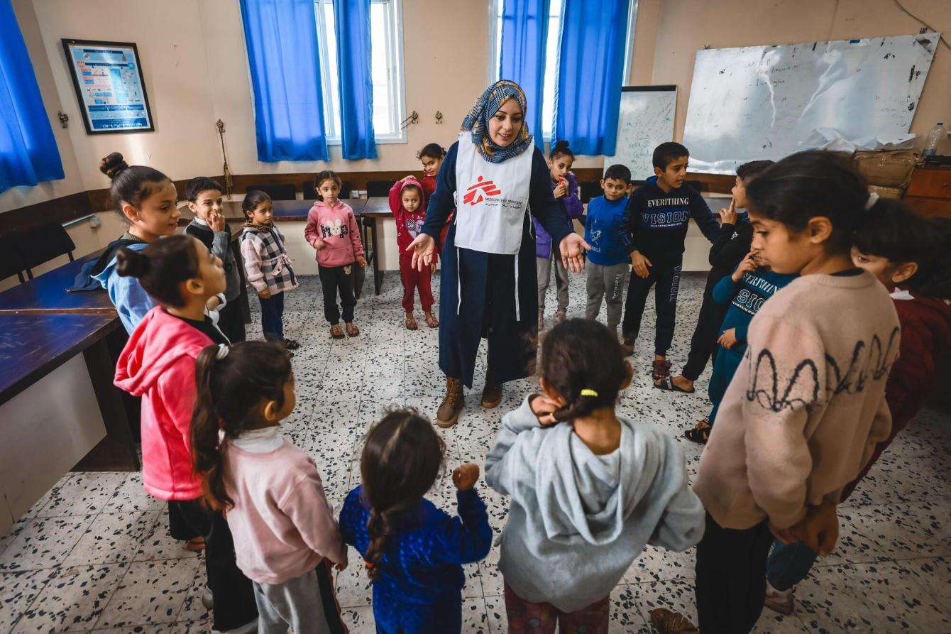 An MSF psychologist stands at the center of a circle of Palestinian children in a mental health session in Gaza.