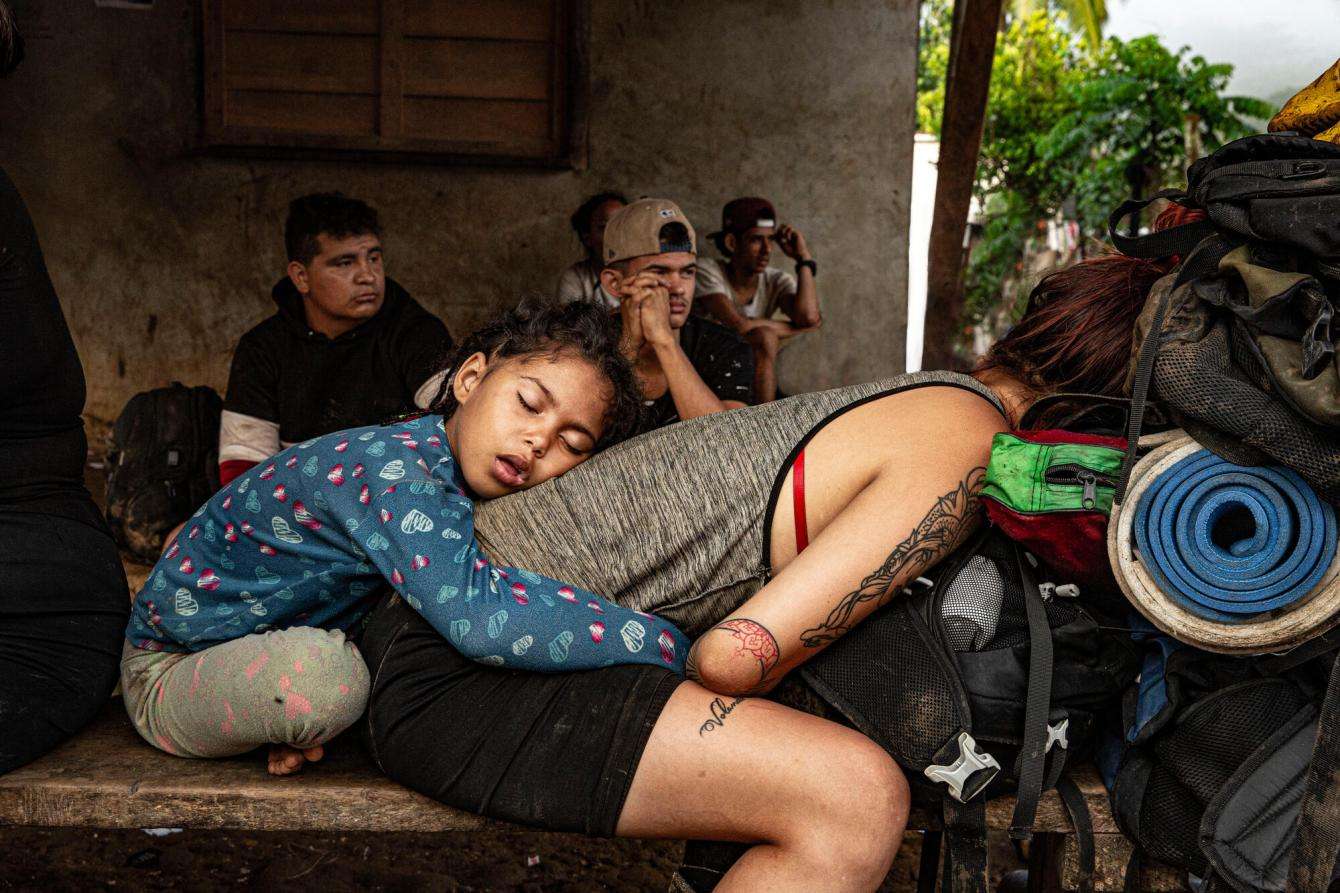 A child sits behind his mother who is crouching down on a bench after crossing the Darién Gap.