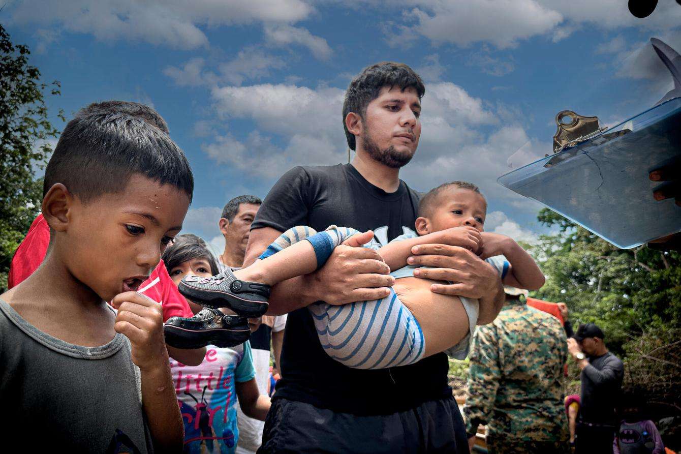 A migrant carries a small child with another beside him as he crosses the Darién Gap between Colombia and Panama.