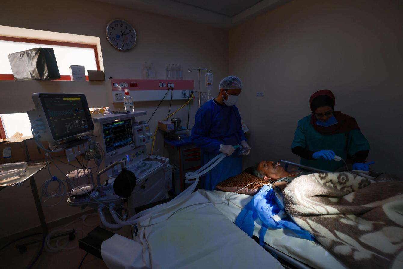 Doctors perform surgery on a patient in a dark room lit by a window at Al Aqsa Hospital in Gaza