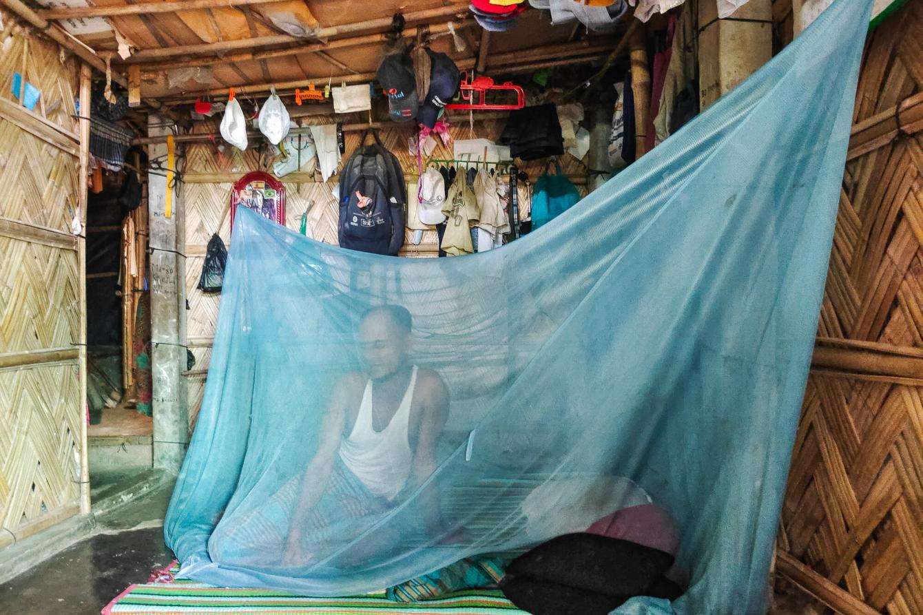 A Rohingya man behind a blue mosquito net in Cox's Bazar, Bangladesh.