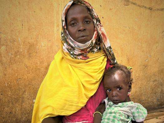 A Sudanese refugee woman in a yellow scarf holds her child in Chad, after fleeing there for safety.
