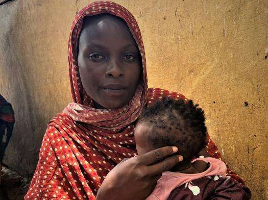 A Sudanese refugee woman in a red scarf holding her child after fleeing to Chad for safety.