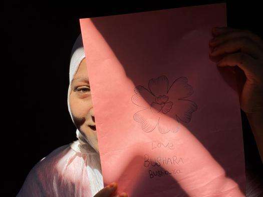A Rohingya girl holding a drawing over her face.