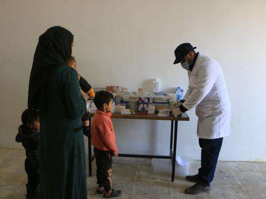 A mother and child are standing by a table full of pharmaceuticals as a medic reaches for something on the table.