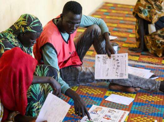 Two men who work for MSF sit on the floor reviewing health literature at the Abukadra mobile clinic, Upper Nile state. 
