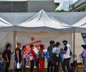 A group of migrants standing on a line under an MSF tent in Danlí, Honduras.