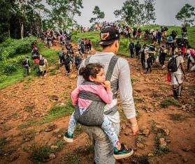 A migrant carries a child in a backpack as he crosses the Darién jungle between Colombia and Panama.